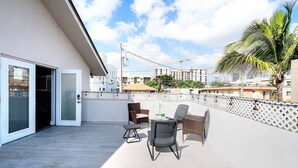 A balcony with outdoor furniture, a palm tree, and a view of other buildings.