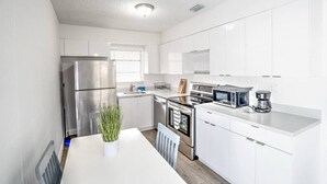 A modern kitchen with white cabinets, stainless steel appliances, a dining table, and a potted plant.