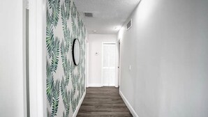 A hallway with a patterned wallpaper, a wooden floor, and a door at the end.