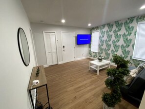 Ein modernes Wohnzimmer mit Holzboden, einem weißen Sofa, einem Couchtisch, einem an der Wand montierten Fernseher und einer Wand mit Muster-Tapete.