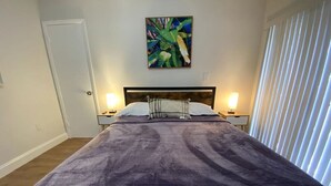 A bedroom with a large bed, two bedside tables with lamps, a door, and a window with blinds. - Renovated 2/1 apt w/ parking near Brickell Center (Miami)