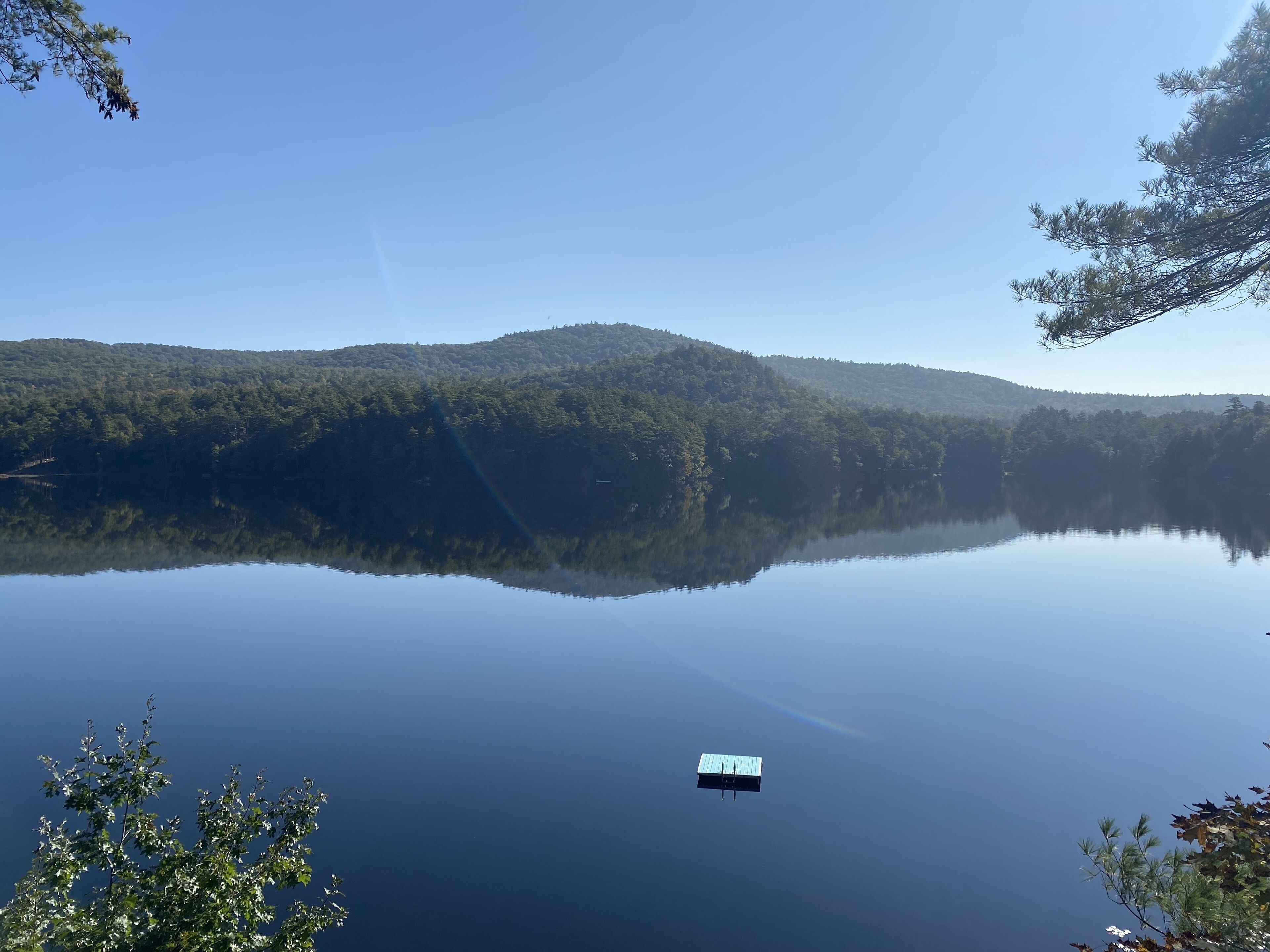 A calm lake with a dock and forested hills in the background.
