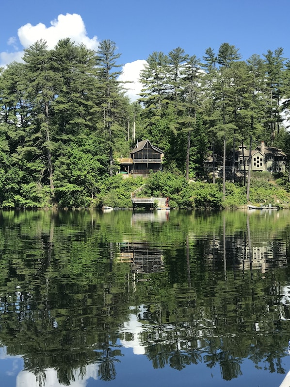 A lakeside cabin with a dock, surrounded by dense forest and reflecting in the calm water.