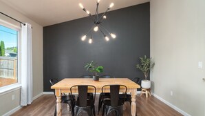 Ein Essbereich mit Holztisch, schwarzen Stühlen, einer Zimmerpflanze und einer modernen Pendelleuchte.