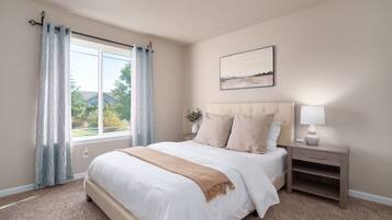 A bedroom with a large bed, a nightstand, a lamp, a window with curtains, and a painting on the wall.