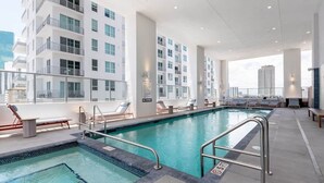 Une piscine sur le toit offrant une vue sur un immeuble moderne, des chaises longues et un panneau indiquant qu’il est interdit de plonger.