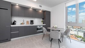 Une cuisine moderne avec des meubles gris, un plan de travail blanc et un coin repas comprenant une table ronde et des chaises.