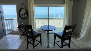 A room with a balcony overlooking the ocean, featuring a round table and two chairs, a ceiling fan, and a view of the sea. - Beachside condo #B with 2bd /2 bath (Carlsbad)