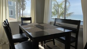A dining area with a table and chairs, large windows with curtains, and a view of the beach and ocean. - Beachside condo #B with 2bd /2 bath (Carlsbad)