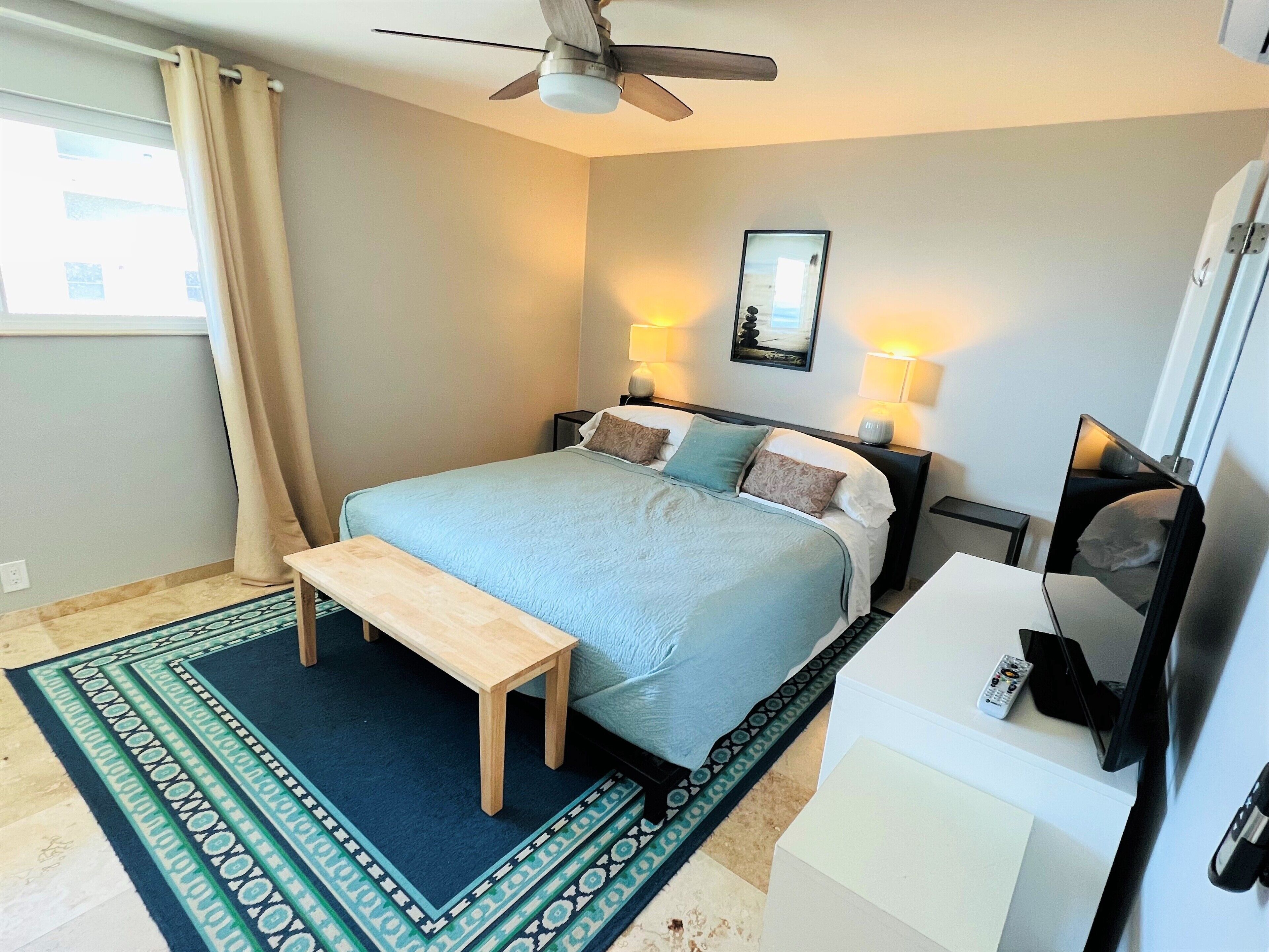 A neatly arranged bedroom with a bed, bedside lamps, a ceiling fan, a bedside table, and a TV.