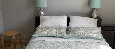 A bedroom with a bed, two bedside lamps, a small stool, and a wall-mounted painting.
