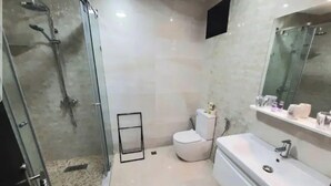 Ein modernes Badezimmer mit einer gläsernen Duschkabine, einer weißen Toilette und einem großen Spiegel über dem Waschbecken.