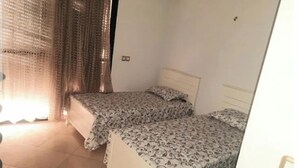 Ein Zimmer mit zwei Betten, einem fenster mit Vorhängen und einem Fliesenboden.