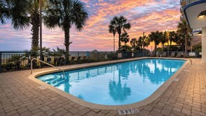 A swimming pool with a sunset view, surrounded by palm trees and a fence.