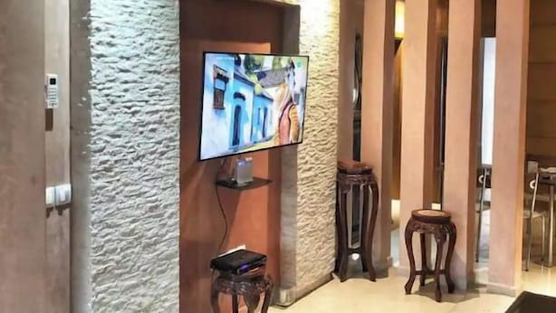 Una sala de estar moderna con un televisor de pantalla plana montado en una pared texturizada, una pequeña mesa de madera y un reposapiés negro.