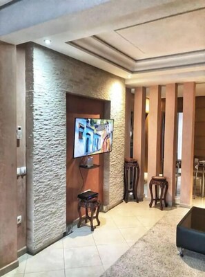 Una sala de estar moderna con un televisor de pantalla plana montado en una pared texturizada, una pequeña mesa de madera y un reposapiés negro.