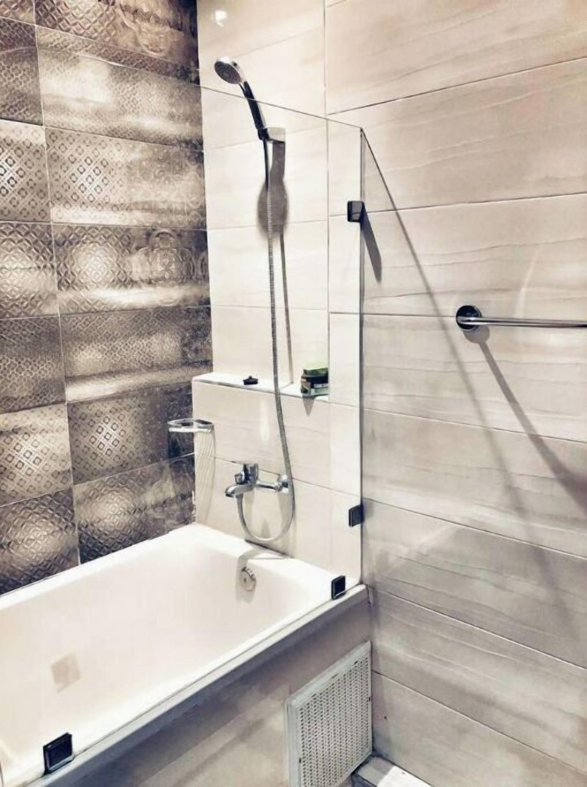 Une salle de bain moderne équipée d’une baignoire, d’une douche avec un pommeau de douche amovible et d’un porte-serviettes fixé au mur.