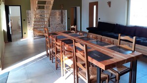 Un vaste espace de vie comprenant une table et des chaises en bois pour la salle à manger, un canapé foncé et un mur en pierre.