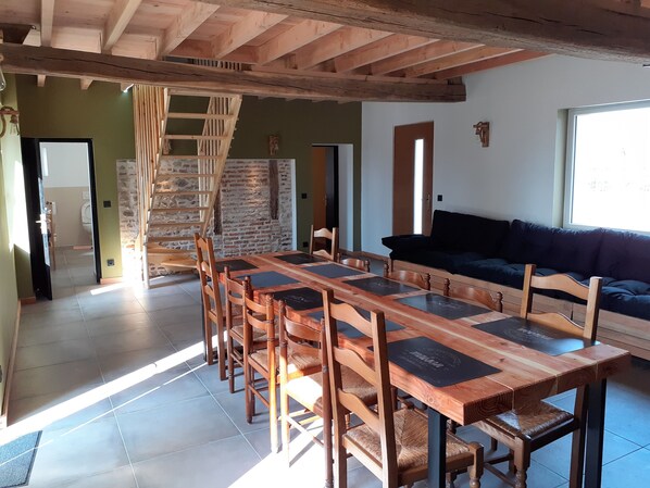 Amplia sala de estar con una mesa y sillas de madera, un sofá oscuro y una pared de piedra.