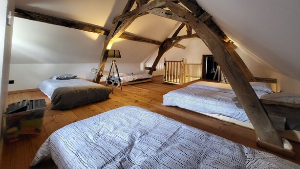 Une chambre confortable située sous les toits, avec des poutres apparentes, deux lits, une petite table et une lampe.