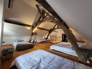 Un dormitorio acogedor en el ático con vigas de madera a la vista, dos camas, una mesita y una lámpara.