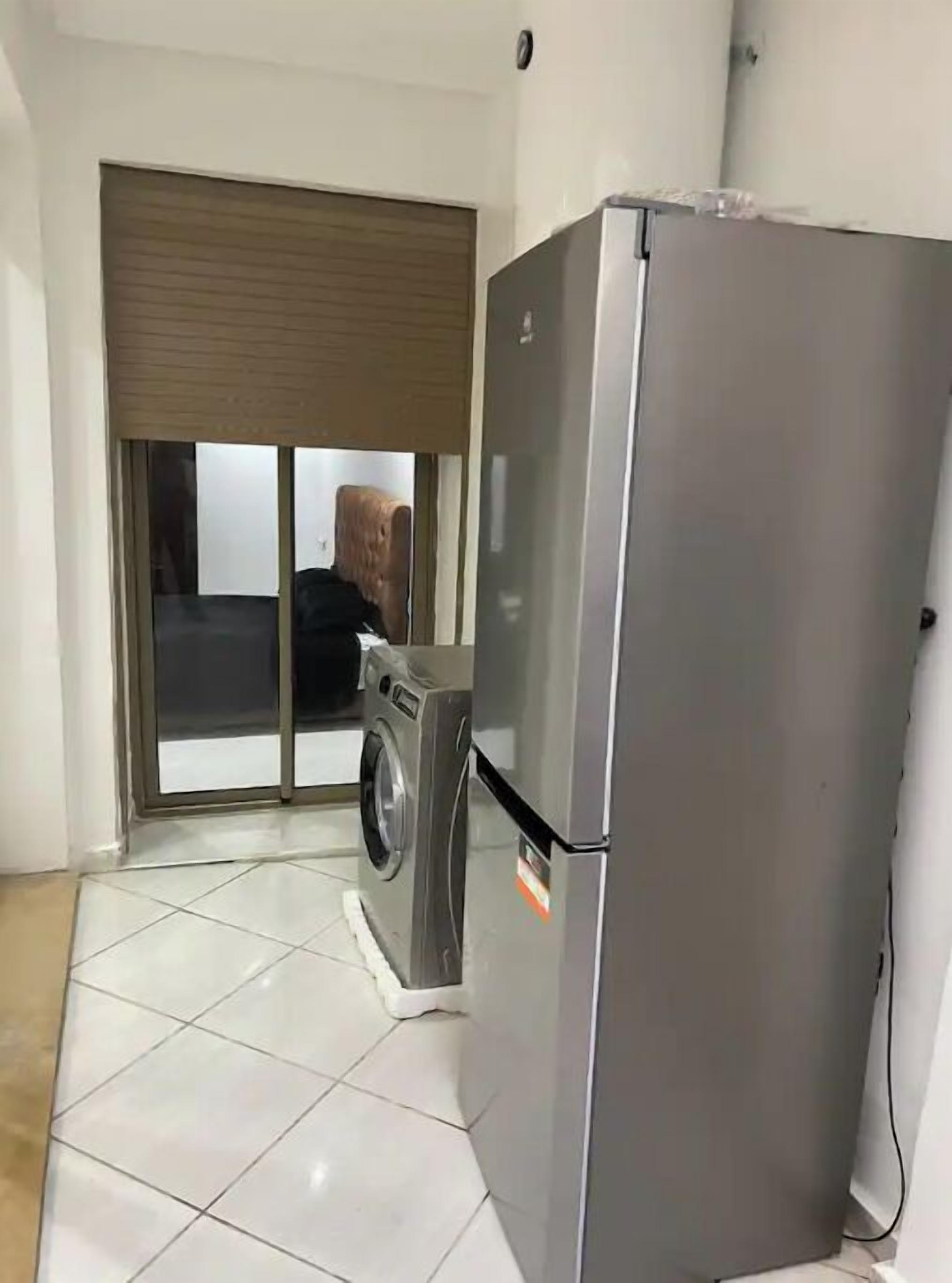 Eine kompakte Küche mit Edelstahl-Kühlschrank, Waschmaschine und einer Schiebeglastür, die auf einen Balkon führt.