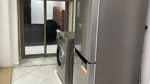 Cocina compacta con refrigerador de acero inoxidable, lavadora y puerta corrediza de vidrio que da a un balcón.