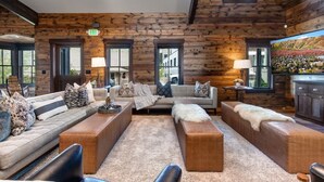A log cabin interior with a sofa set, ottomans, and a fireplace.