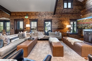 A log cabin interior with a sofa set, ottomans, and a fireplace.
