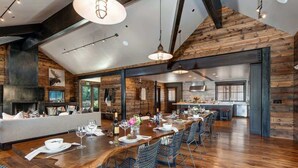 A spacious dining area with a long wooden table, metal chairs, and pendant lighting.