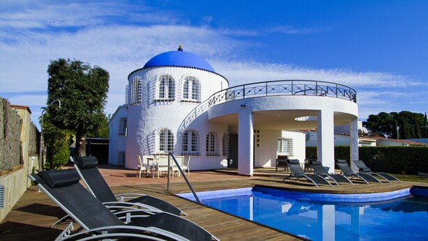 A pool area with lounge chairs, a white building with a blue dome, and a clear sky.