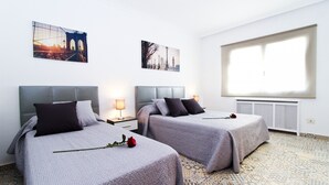 A hotel room with two beds, a large window, and artwork on the walls.