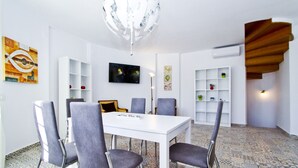 A dining area with a white table and grey chairs, a chandelier, and patterned floor tiles.