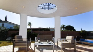 An outdoor patio with a covered seating area, a pool, and a view of a house in the background.