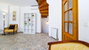 A room with patterned floor tiles, a wooden door, a white shelving unit with decorative items, and a yellow armchair.