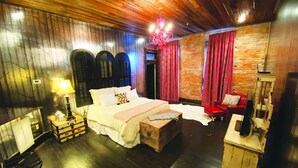 A bedroom with a large bed, wooden headboard, a chandelier, a red chair, and a wooden chest. - MULBERRY (Tishomingo)