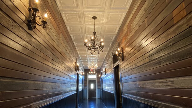 A long, narrow hallway with wooden paneling on the walls and a reflective floor. A chandelier hangs from the ceiling, and wall sconces provide additional lighting. - MULBERRY (Tishomingo)