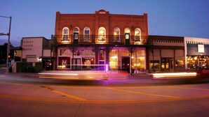 A historic building with a prominent 'M' sign, a covered front porch, and a street view at dusk. - MULBERRY (Tishomingo)