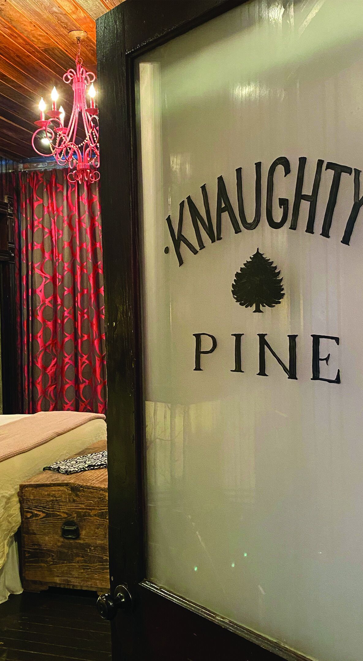 Uma placa emoldurada com o texto "Knaughty Pine" e o logotipo de um pinheiro, indicando um estabelecimento temático.