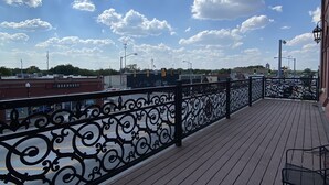 A wooden deck with ornate black railings, a metal table, and a view of the cityscape and sky. - MULBERRY (Tishomingo)