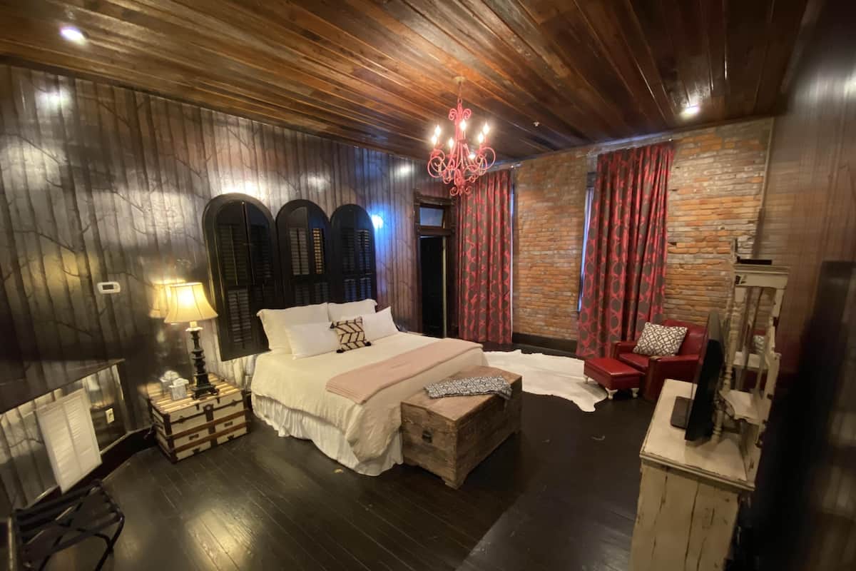 A room with a bed, a red chair, a wooden bench, a lamp, and a chandelier.