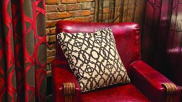 Un sillón tapizado en terciopelo rojo con un cojín estampado, junto a un otoman del mismo diseño, frente a una pared de ladrillo.