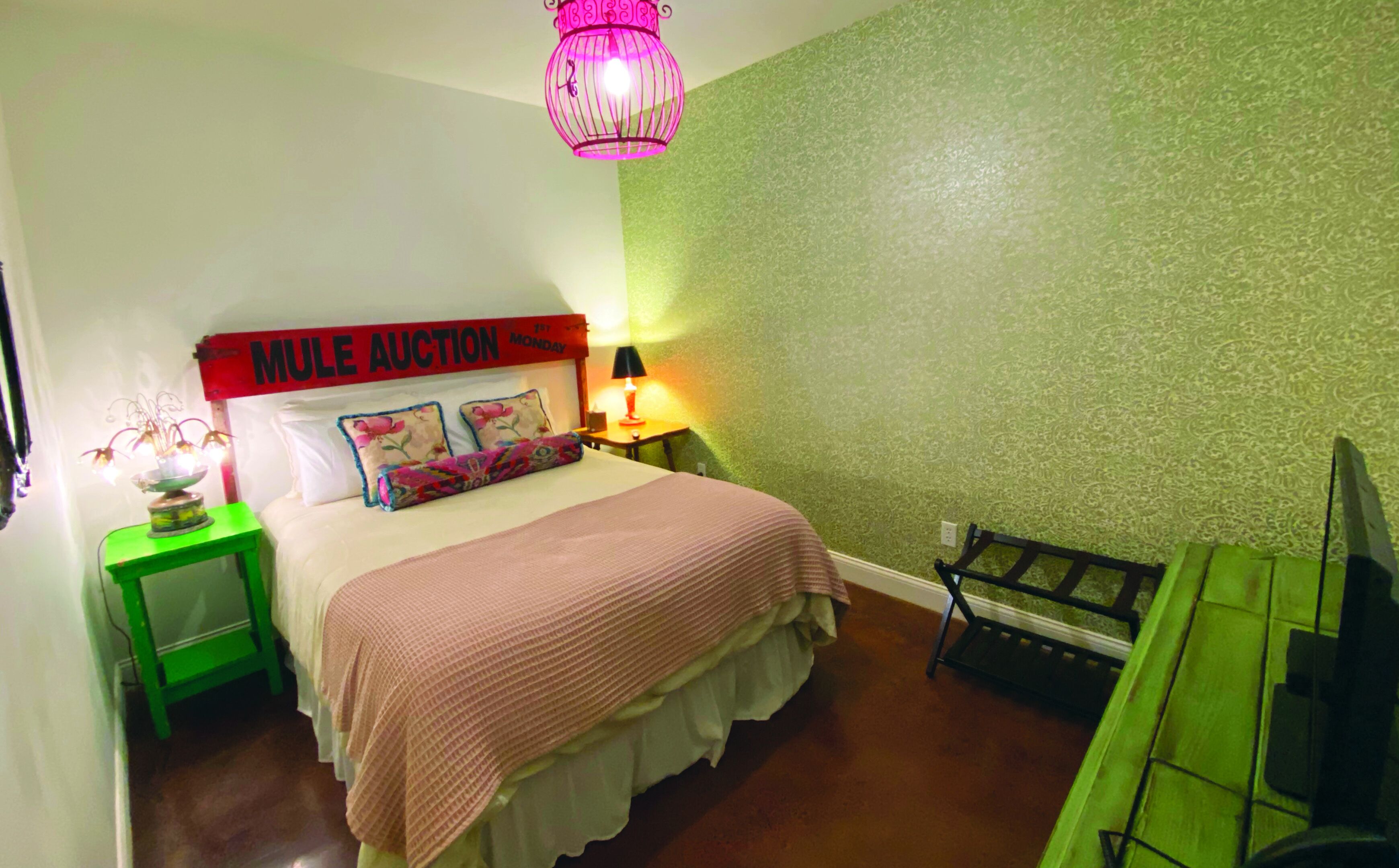 A bedroom with a bed, a nightstand, a lamp, a green chair, and a TV.