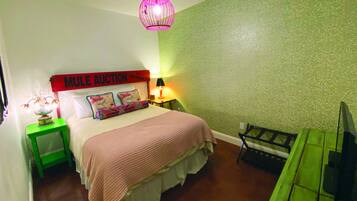 A bedroom with a bed, a nightstand, a lamp, a green chair, and a TV.