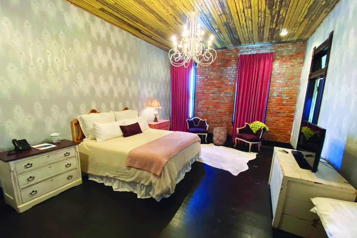 A bedroom with a bed, dresser, chair, and a television.