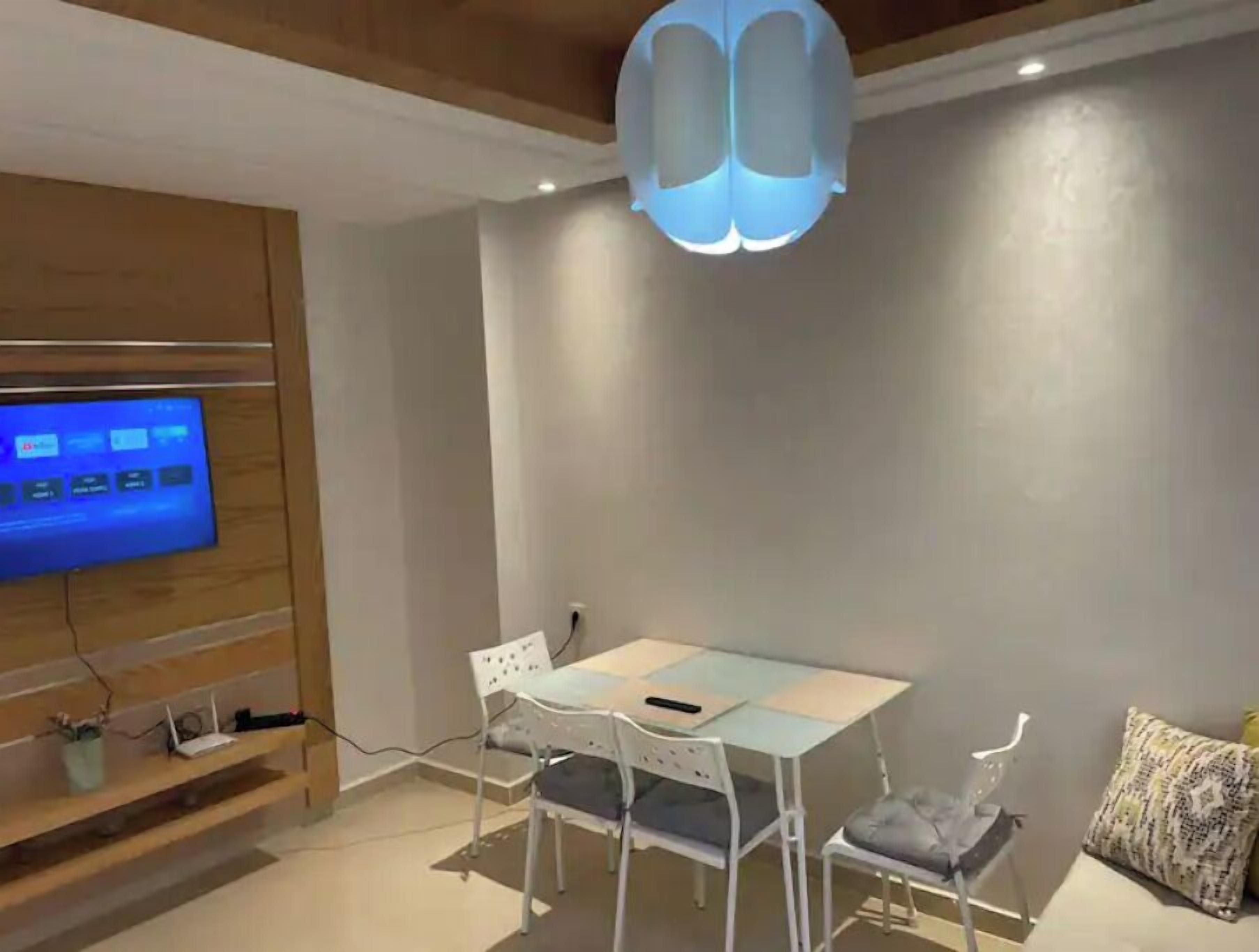 A modern dining area with a glass table, white chairs, and a ceiling light fixture.