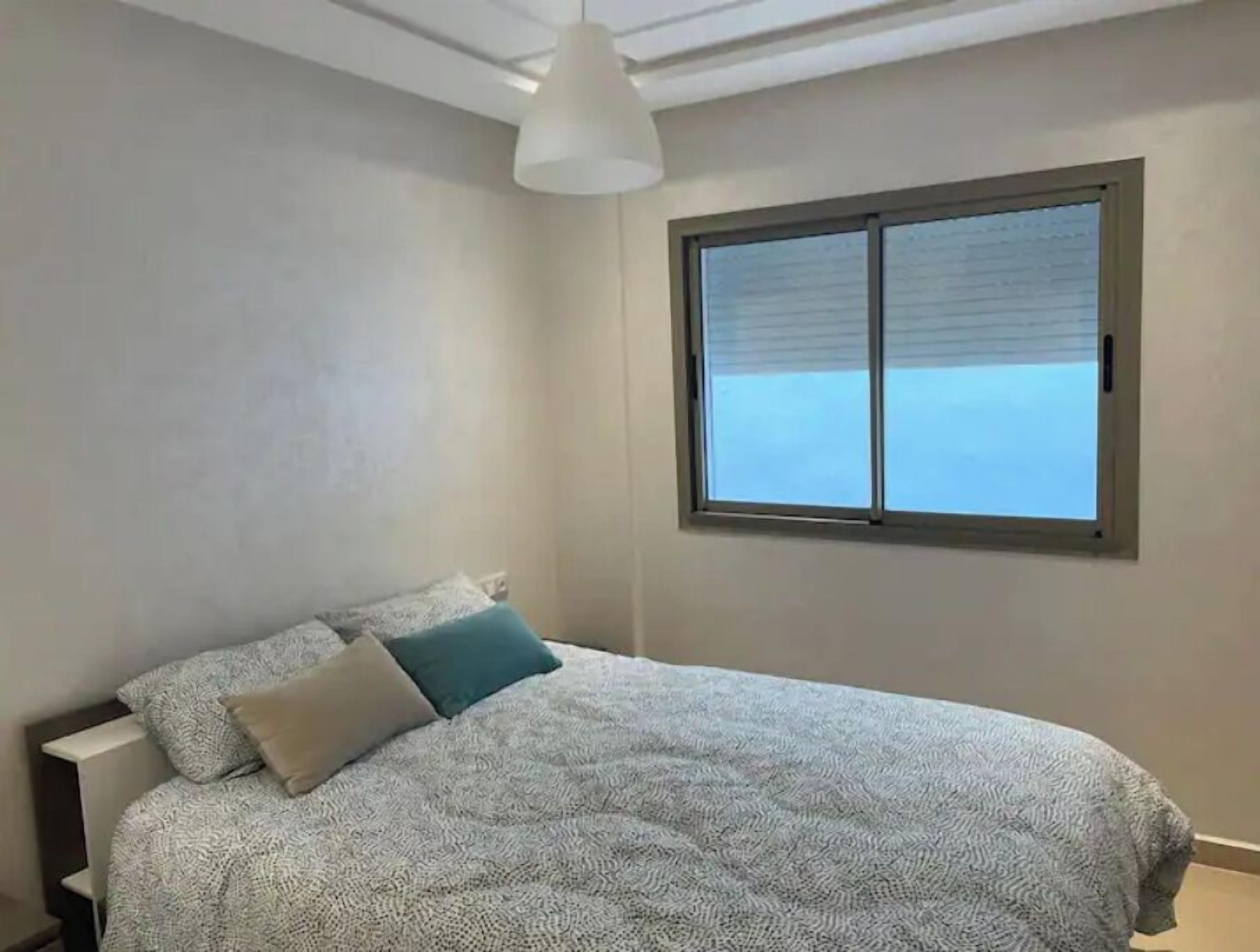 Un dormitorio con cama, ventana y una lámpara en el techo.