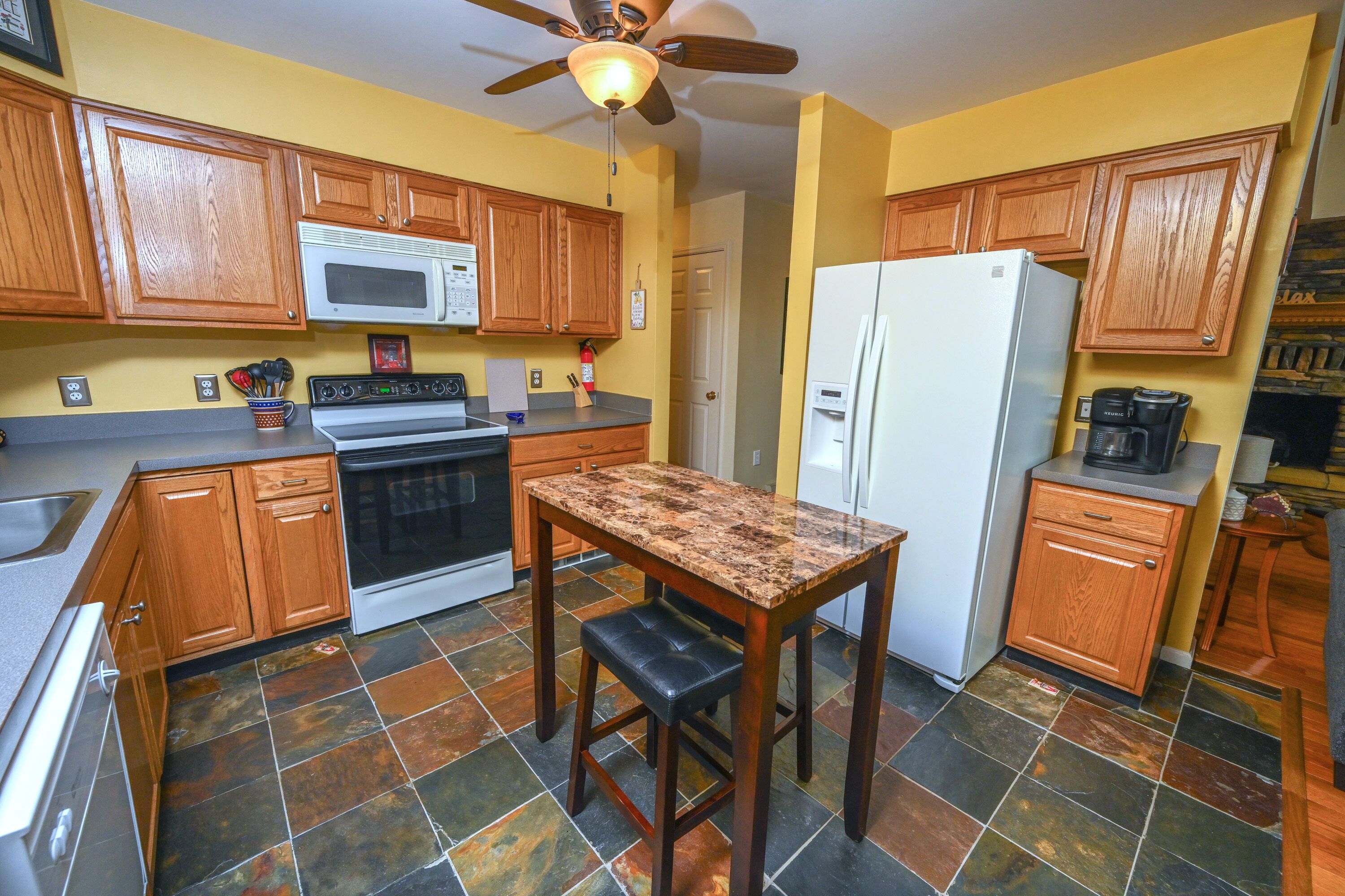 A kitchen with wooden cabinets, a microwave, stove, refrigerator, and a granite countertop.