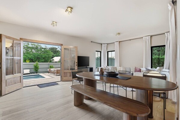 A spacious living area with a large wooden table, a sofa set, and a TV.