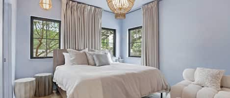 A bedroom with a large bed, two windows, a chandelier, and a sofa.